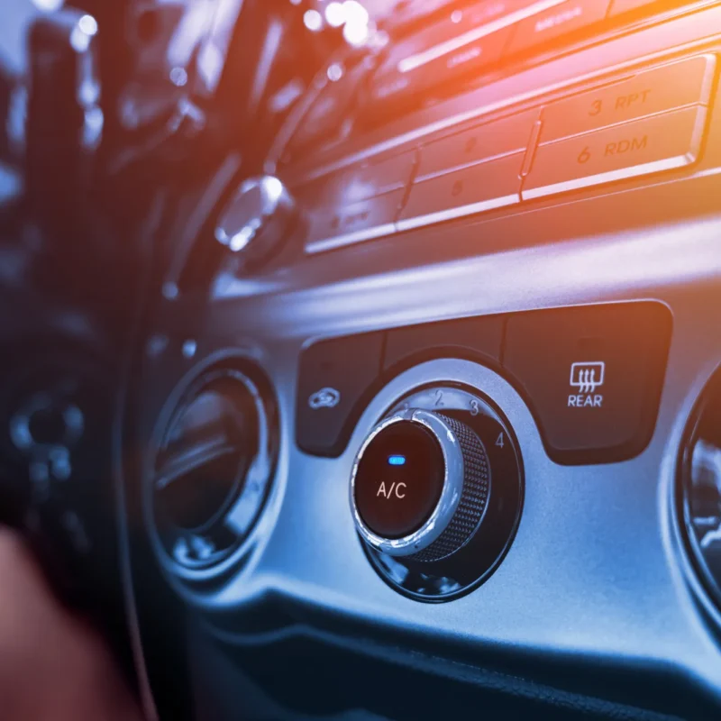 Close-up of a car dashboard's air conditioning control knob labeled A/C with a blue indicator light, next to round air vents and the stereo panel.