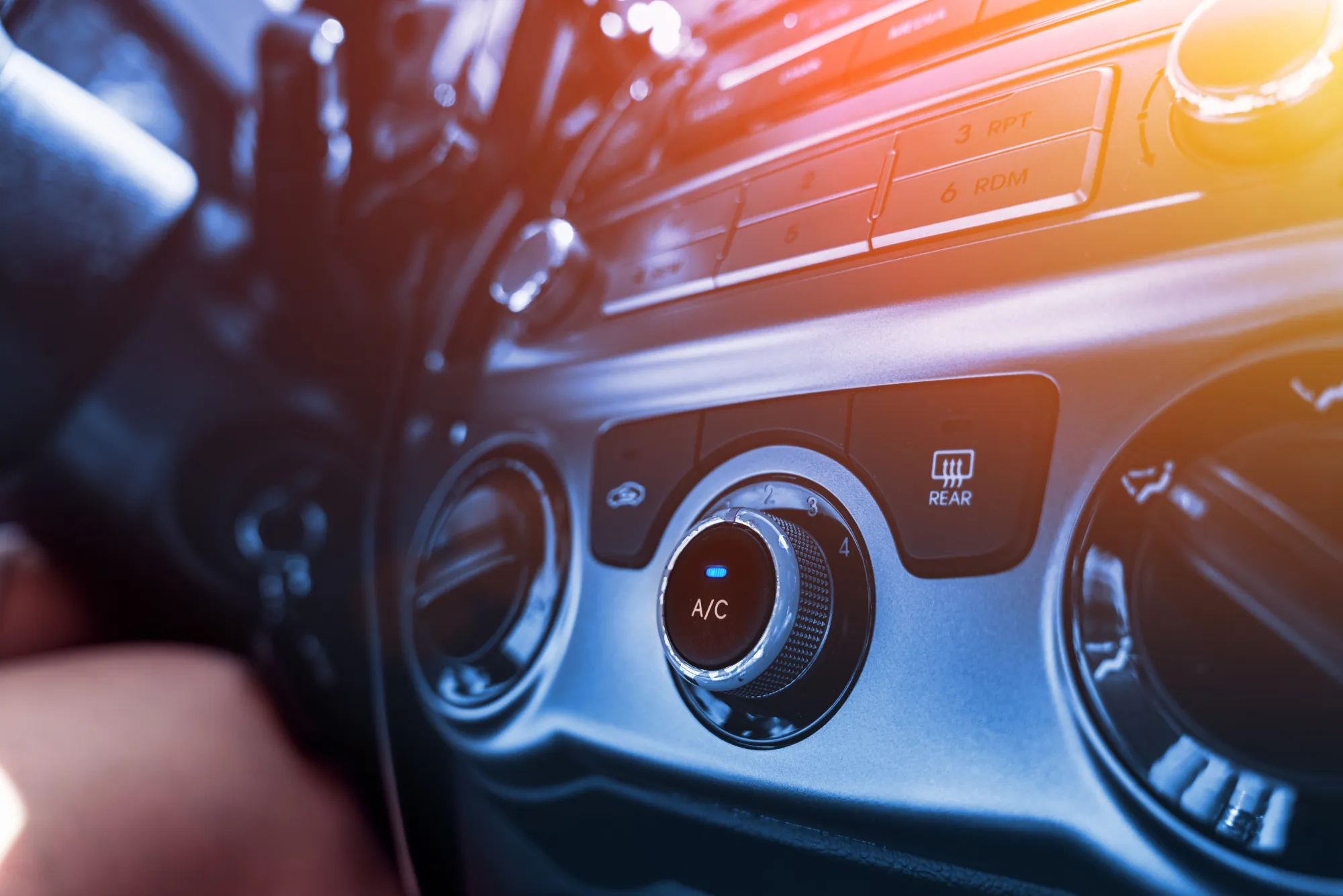 Close-up of a car dashboard's air conditioning control knob labeled A/C with a blue indicator light, next to round air vents and the stereo panel.